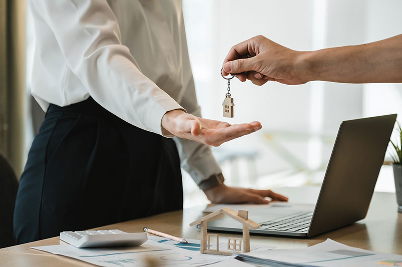 Schlüsselübergabe beim Immobilienverkauf am Schreibtisch mit Laptop und Hausmodell – Immobilie verkaufen Bad Vilbel professionell und sicher abwickeln